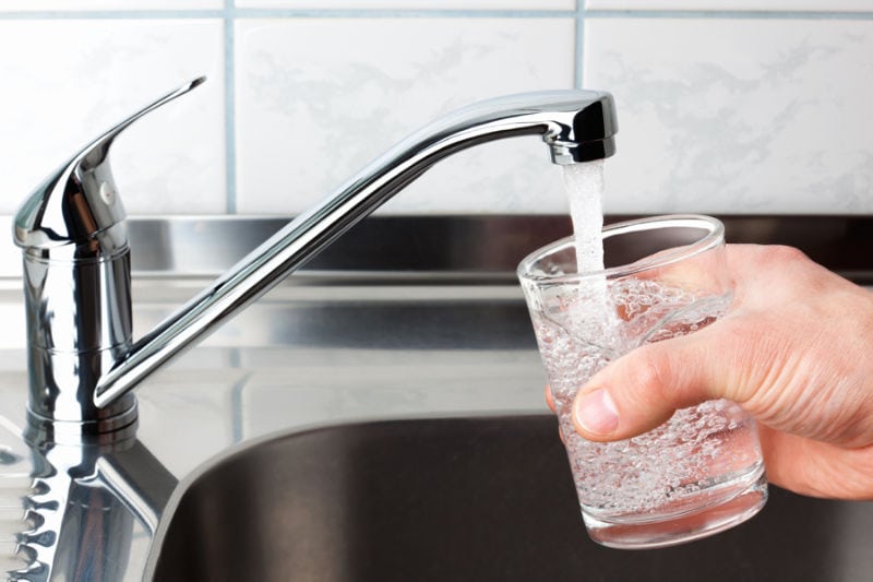Hand holding a glass of water poured from the kitchen faucet.