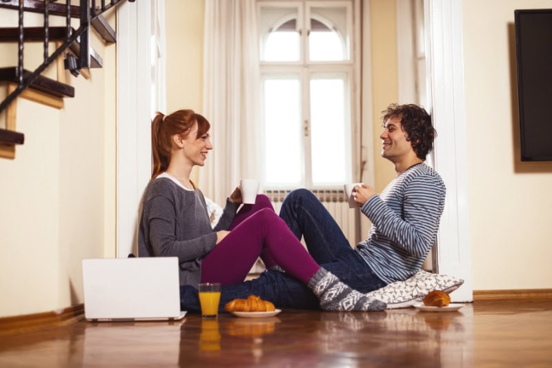 HP_A_018_GettyImages-901621668 How to Determine Heat Pump Efficiency. Couple sitting on the floor drinking out of mugs and eating breakfast.