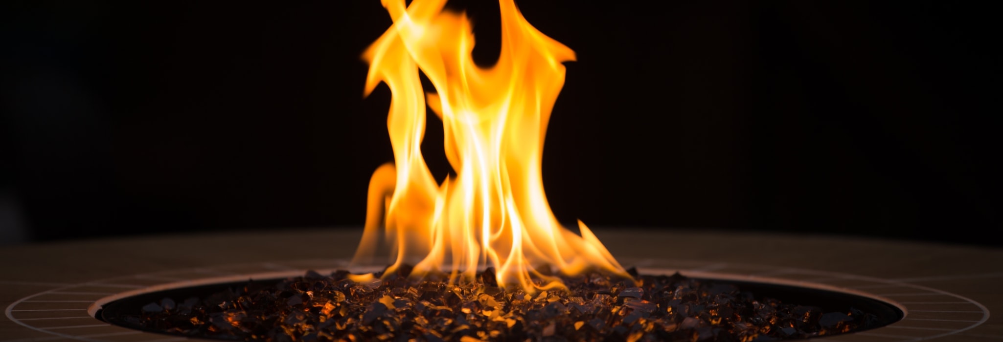 Close up of an outdoor fireplace with a big yellow flame and black background.